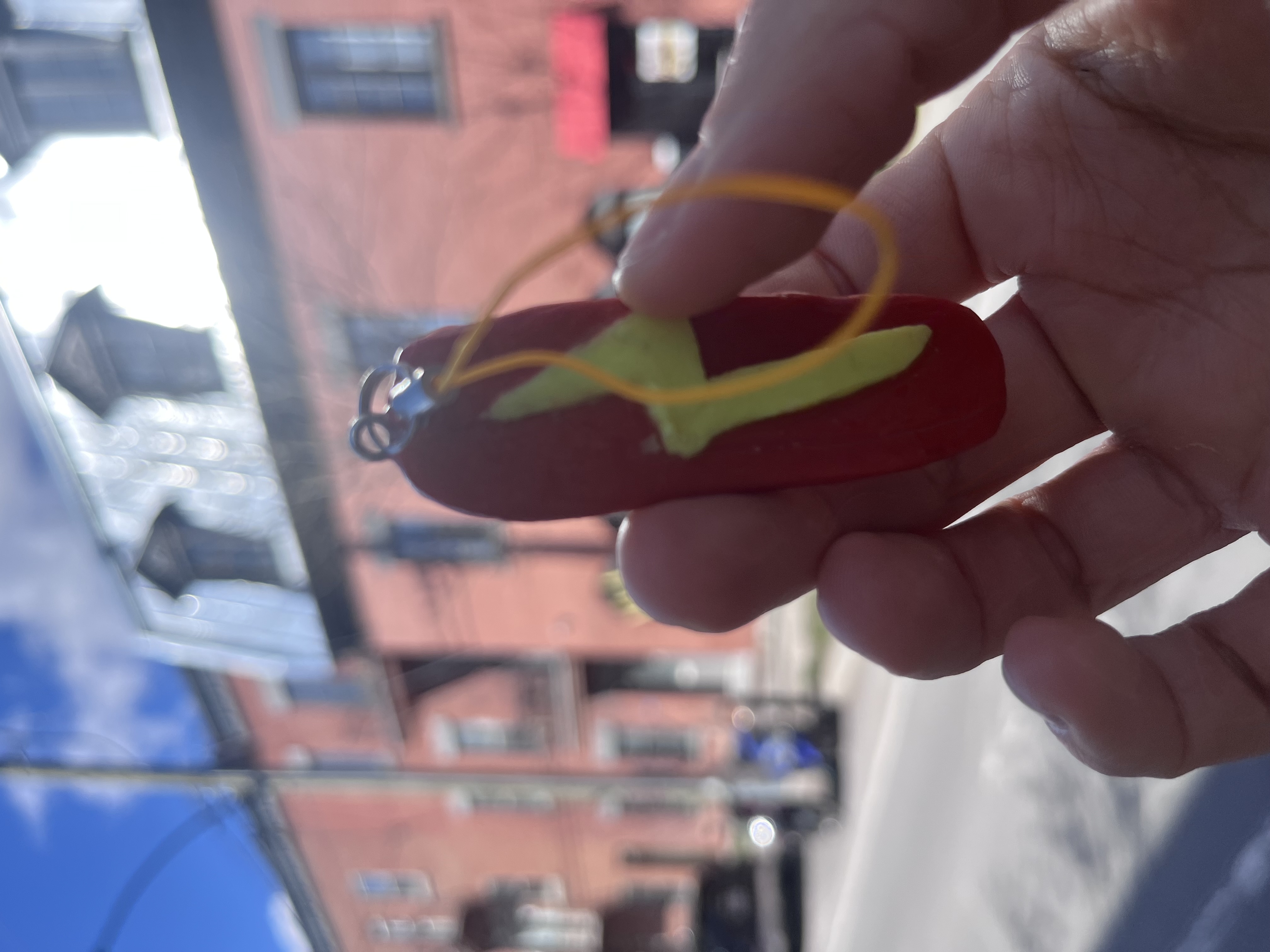 A handmade surfboard keychain, painted red with a yellow lightning bolt
